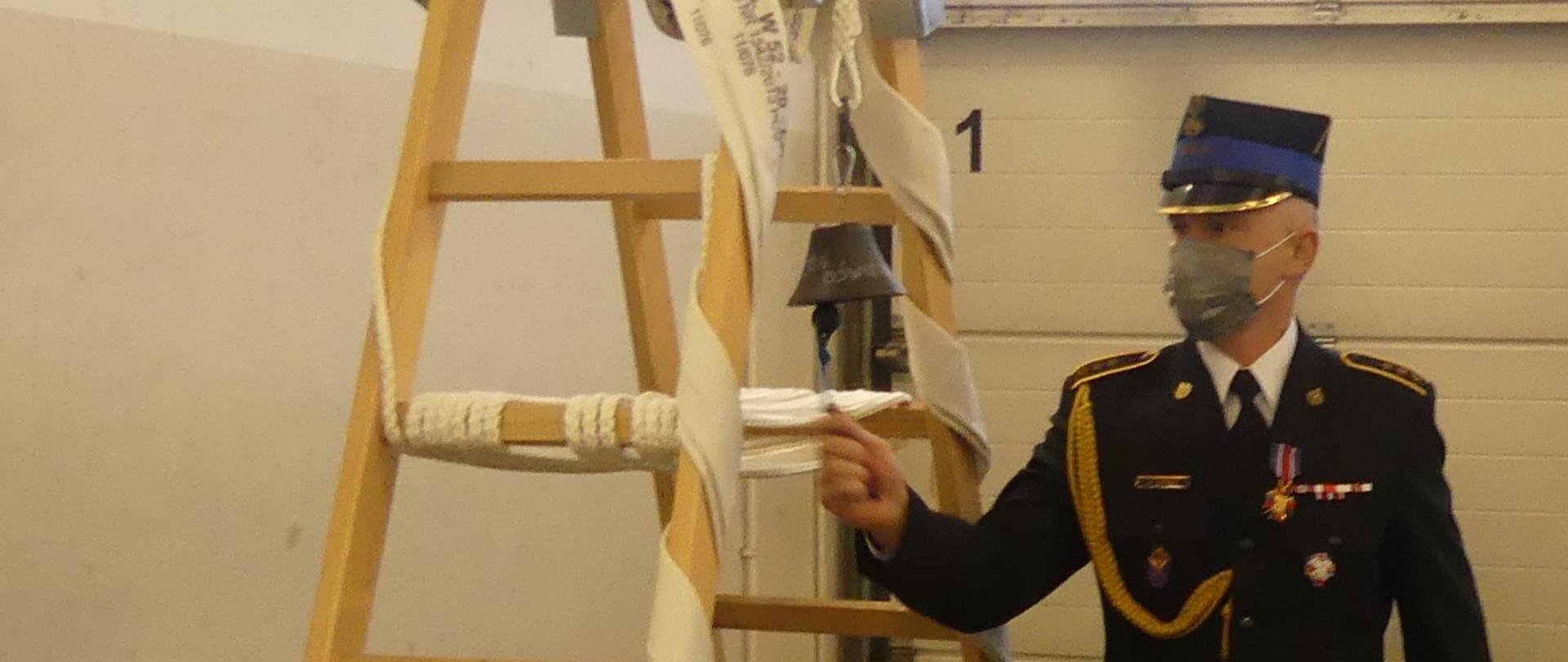 mężczyzna w mundurze bije w mały dzwonek zawieszony na dwóch drabinach