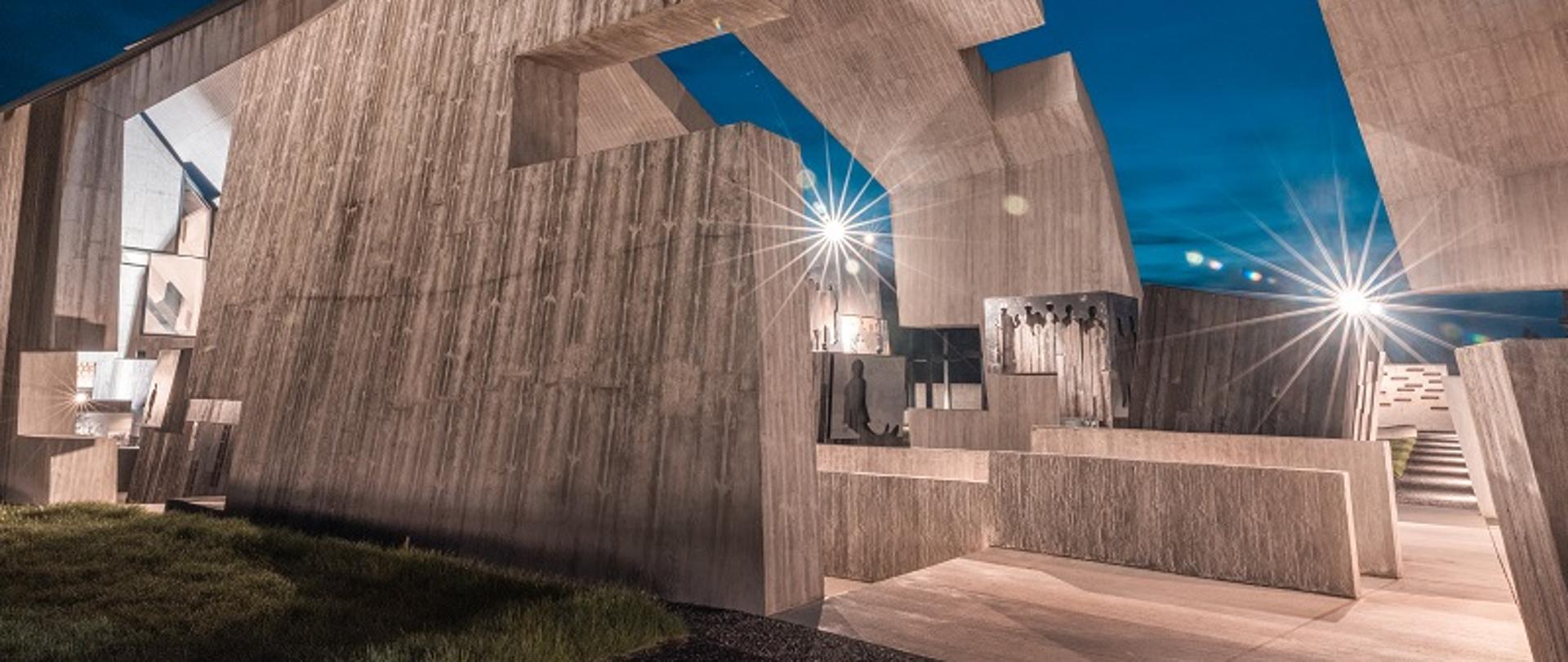 Zdjęcie przedstawia Mauzoleum w Michniowie nocną porą. Są to betonowe bryły o nieregularnym kształcie, przypominającym chatę.