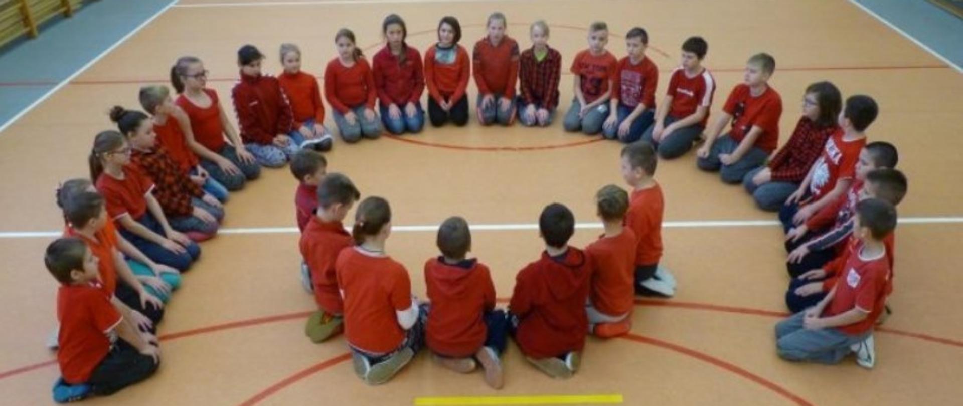 Children in red T-shirts sit on the floor forming the shape of the Polish Aid logo. The inscription "Polish aid" is below.