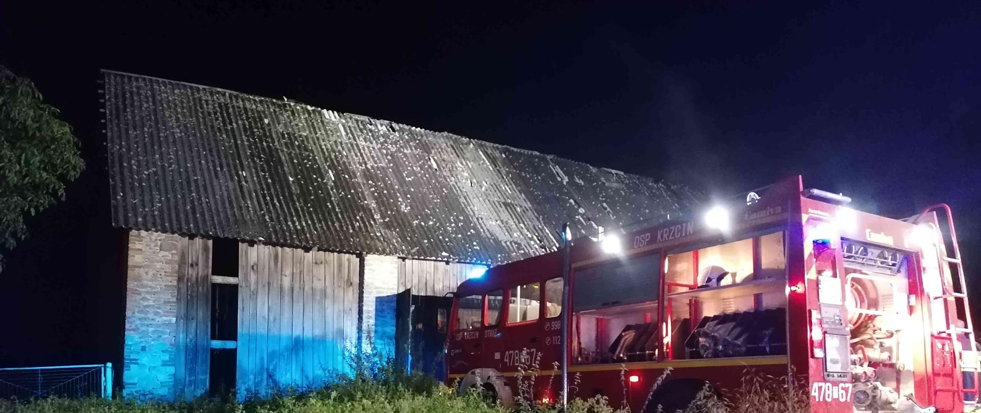 Zdjęcie zrobione w nocy. Na zdjęciu samochód pożarniczy oraz palącą się stodołę. 