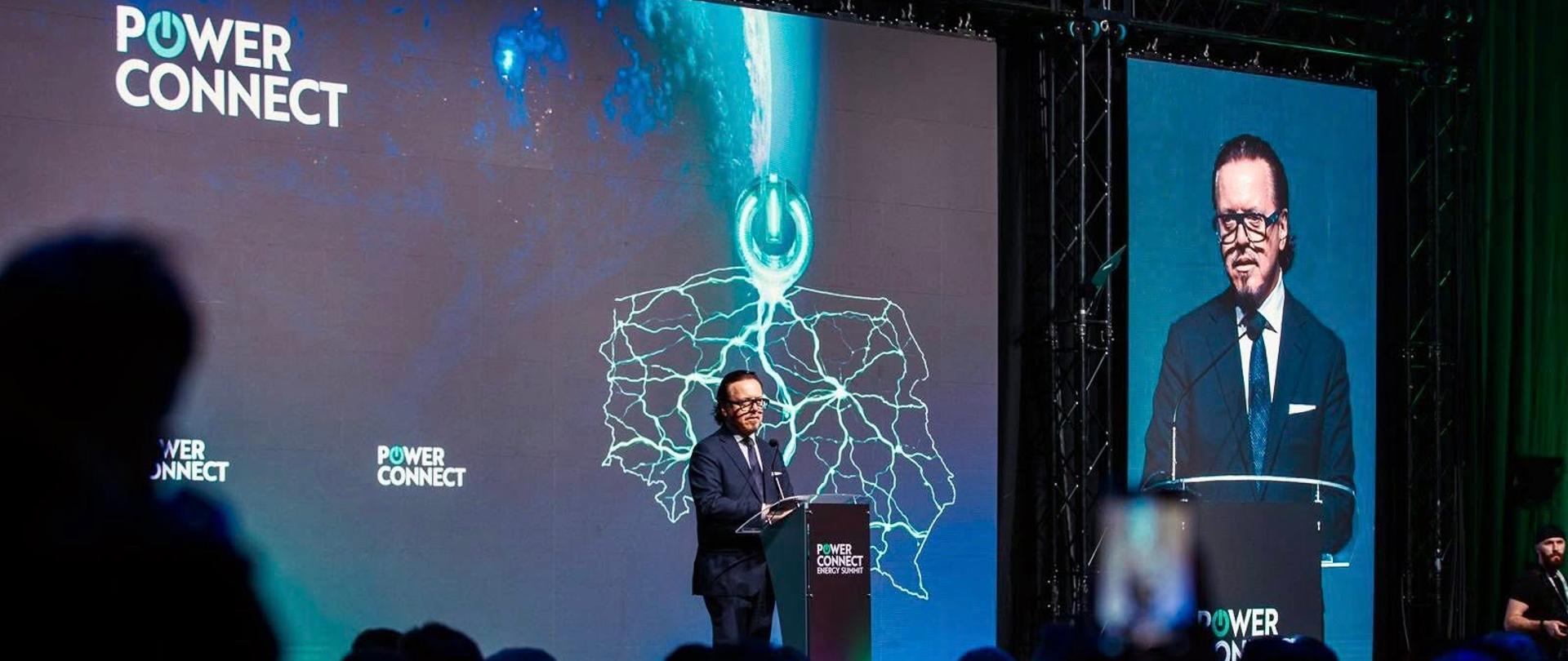 Minister Wojciech Balczun stoi za mównicą. W tle ekran z konturami mapy Polski i napis Power Connect. Ujęcie zza słuchaczy. 