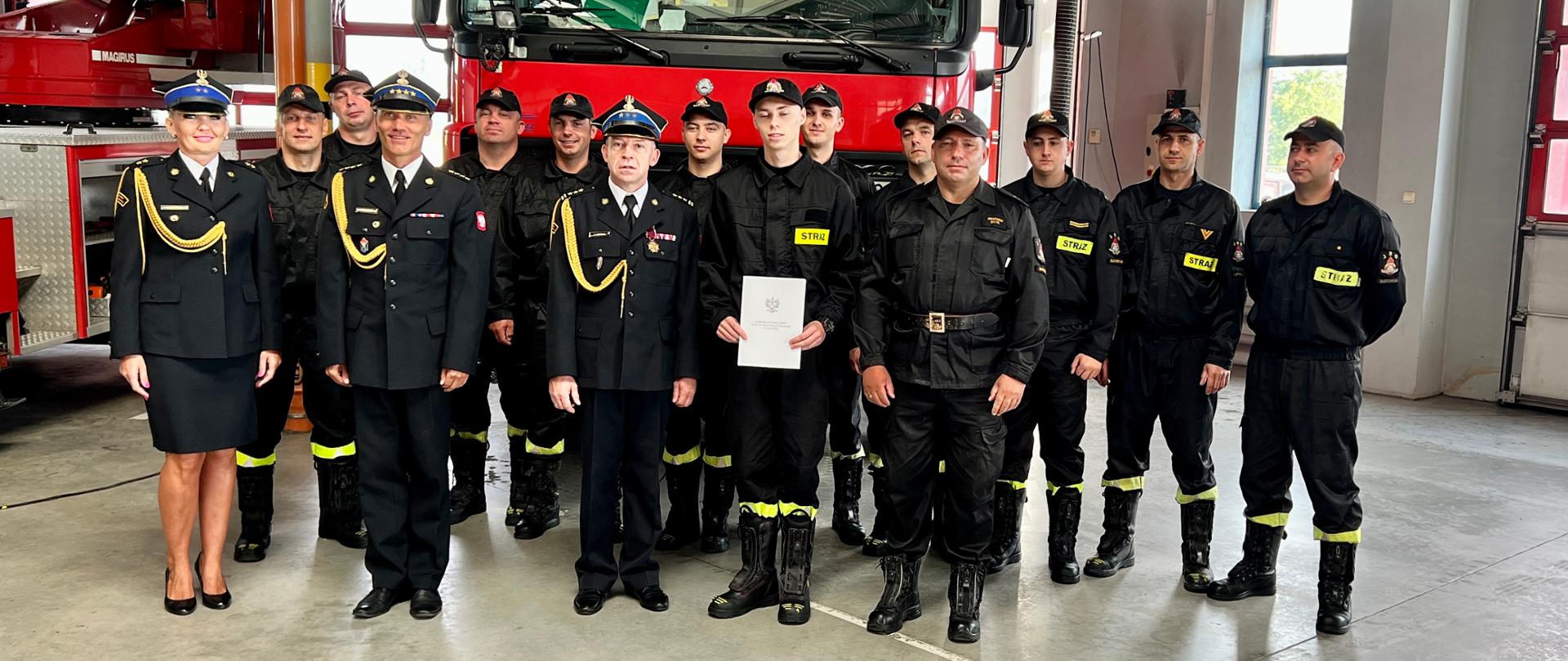 grupa strażaków na tle pojazdu strażackiego w obiekcie garażowym