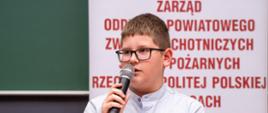Zajęcie przedstawia uczestnika eliminacji powiatowych Ogólnopolskiego Turnieju Wiedzy Pożarniczej w Sali Centrum Kształcenia Zawodowego w Gorlicach siedzącego trzymającego mikrofon i odpowiadającego na pytania konkursowe.