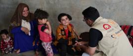 Man with a vest with logos of Polish Aid, Polish Medical Mission, talking with children and women
