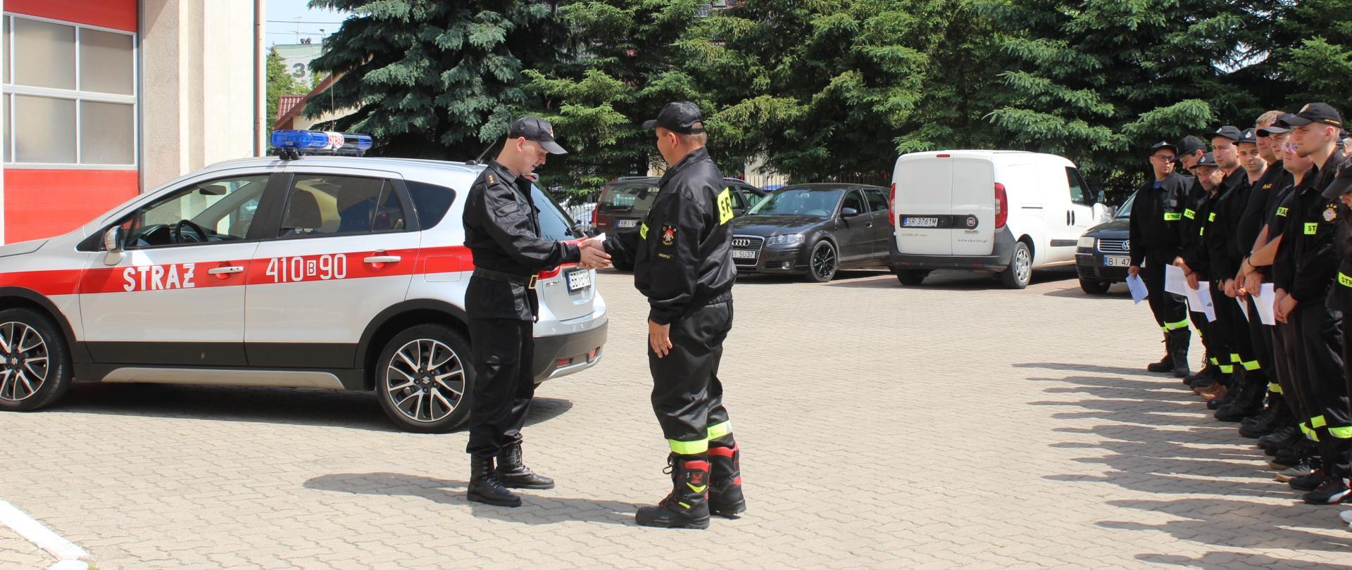 zdjęcie przedstawia funkcjonariusza państwowej straży pożarnej podczas wręczenia druhowi osp zaświadczenia o ukończonym szkoleniu 