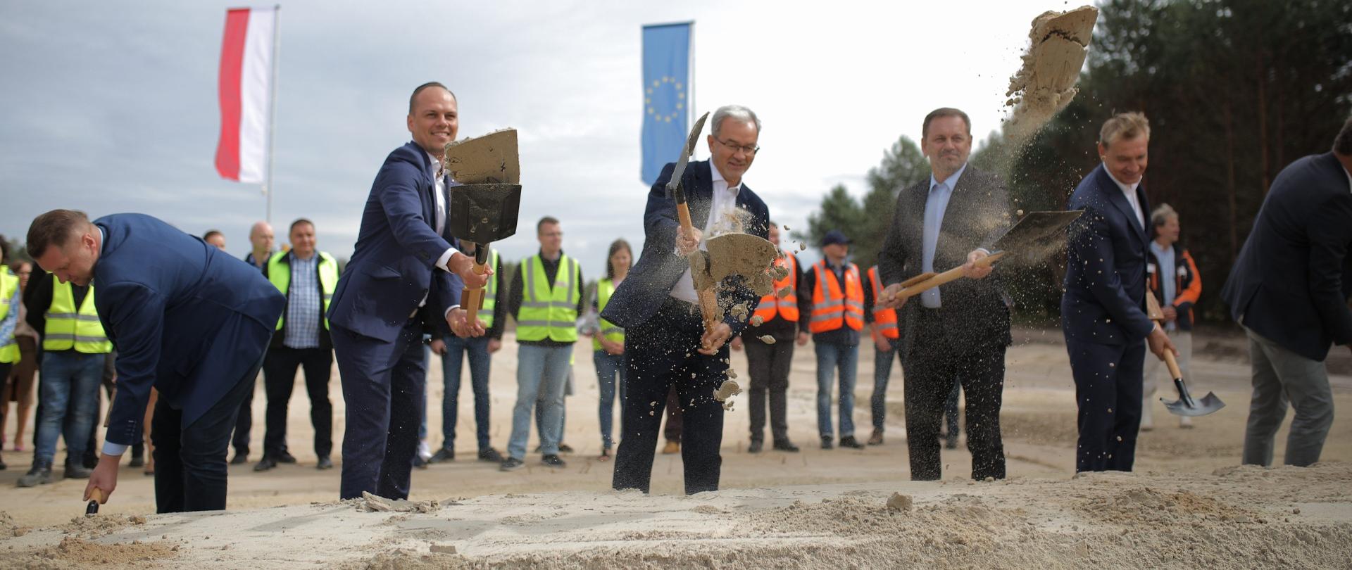 uczestnicy uroczystości wyrzucają łopatami piach w górę