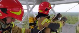 strażacy na kratownicowej metalowej wieży dostrzegalni pożarowej wciągający sprzęt na wysokości ok. 30 m