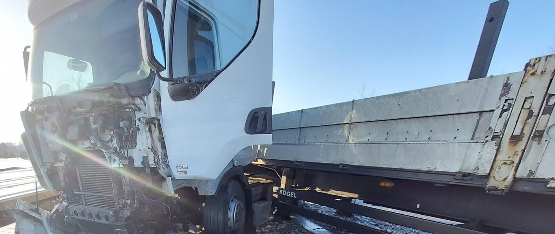 Zdjęcie przedstawia uszkodzony samochód ciężarowy z naczepą po wypadku drogowym. Pojazd stoi w poprzek jezdni blokując przejazd