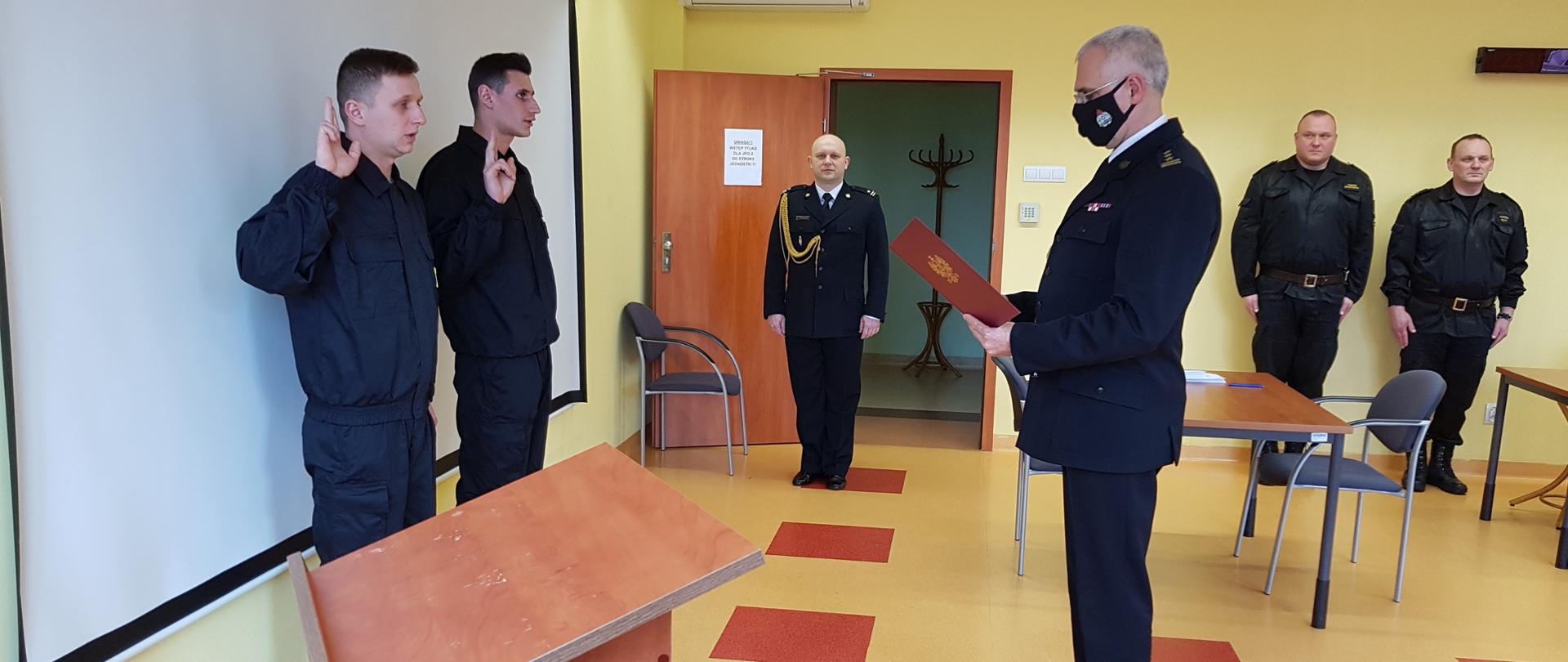 Komendant Miejski PSP w Wałbrzychu czyta tekst ślubowania. Strażacy stojący przed nim mają podniesioną prawą rękę