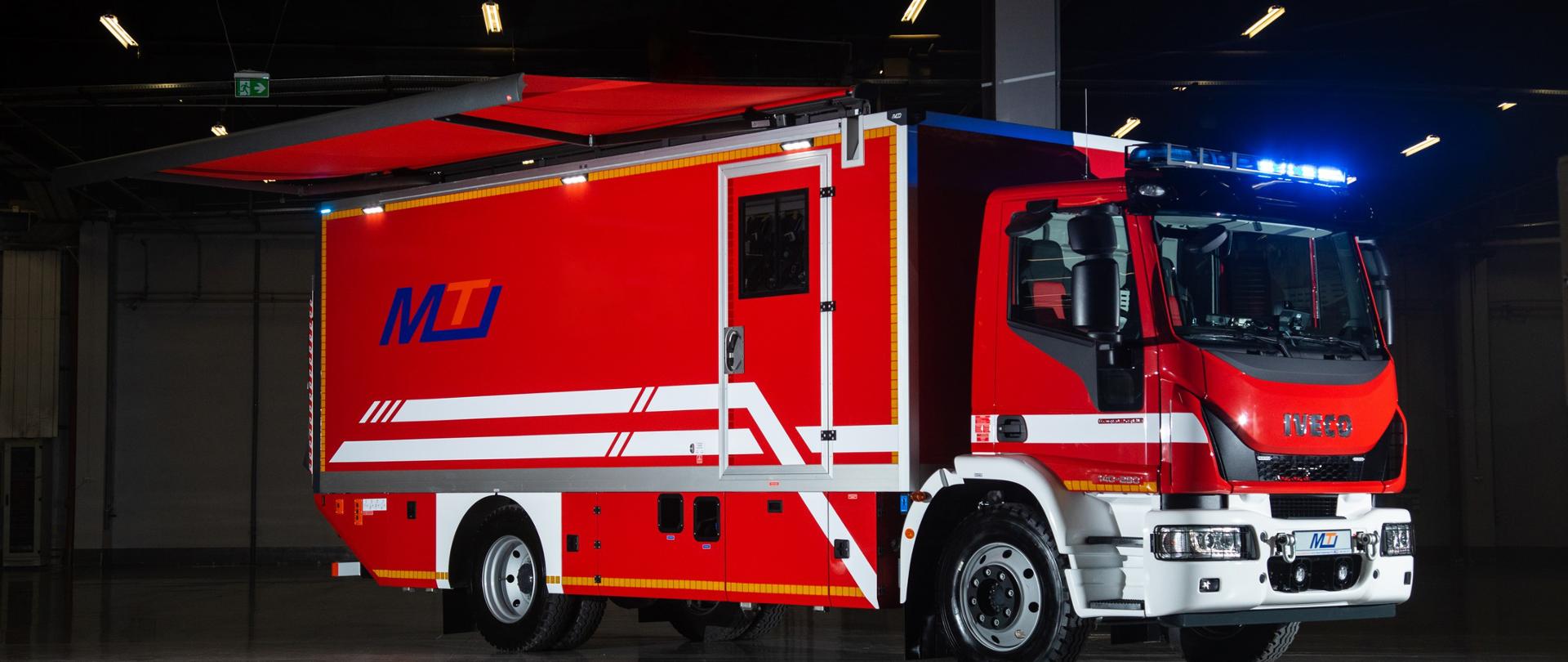 Przód i prawy bok pojazdu specjalnego przeciwgazowego, pojazd koloru czerwonego marki Iveco znajdujący się w hali. 