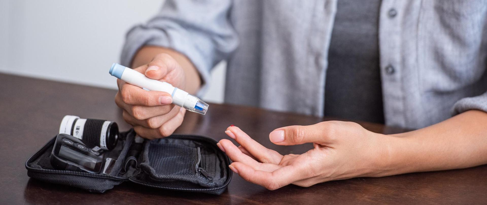 Na zdjęciu jest kobieta. Siedzi przy stole, w dłoniach ma pen insulinowy.