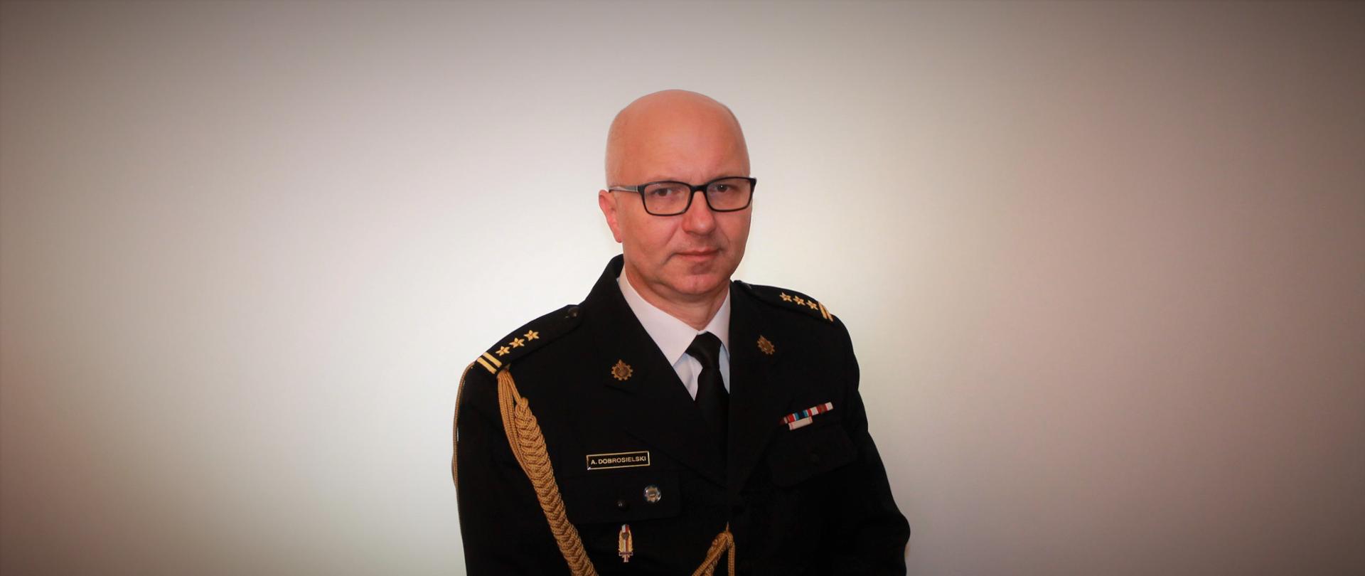 Mężczyzna w okularach siedzi w mundurze i patrzy przed siebie. Za mężczyzną biała ściana.