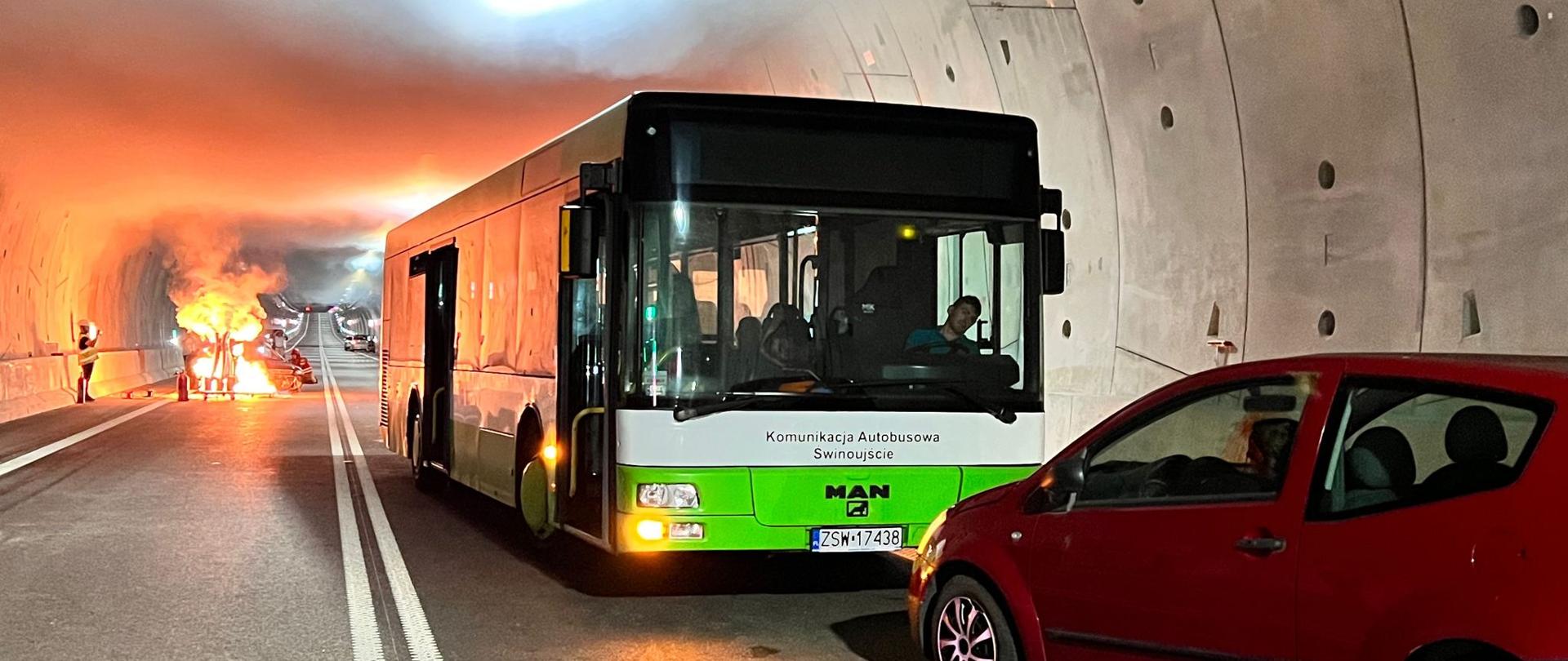 Zdjęcie przedstawia środki pozoracyjne zastosowane podczas ćwiczeń. Na zdjęciu widoczny autobus wraz z samochodem osobowym koloru czerwonego zwrócone frontem do siebie. na drugim planie w oddali widać płomień z tac pozoracyjnych oraz wytwornice dymowe wytwarzające dym w celach pokazowych.