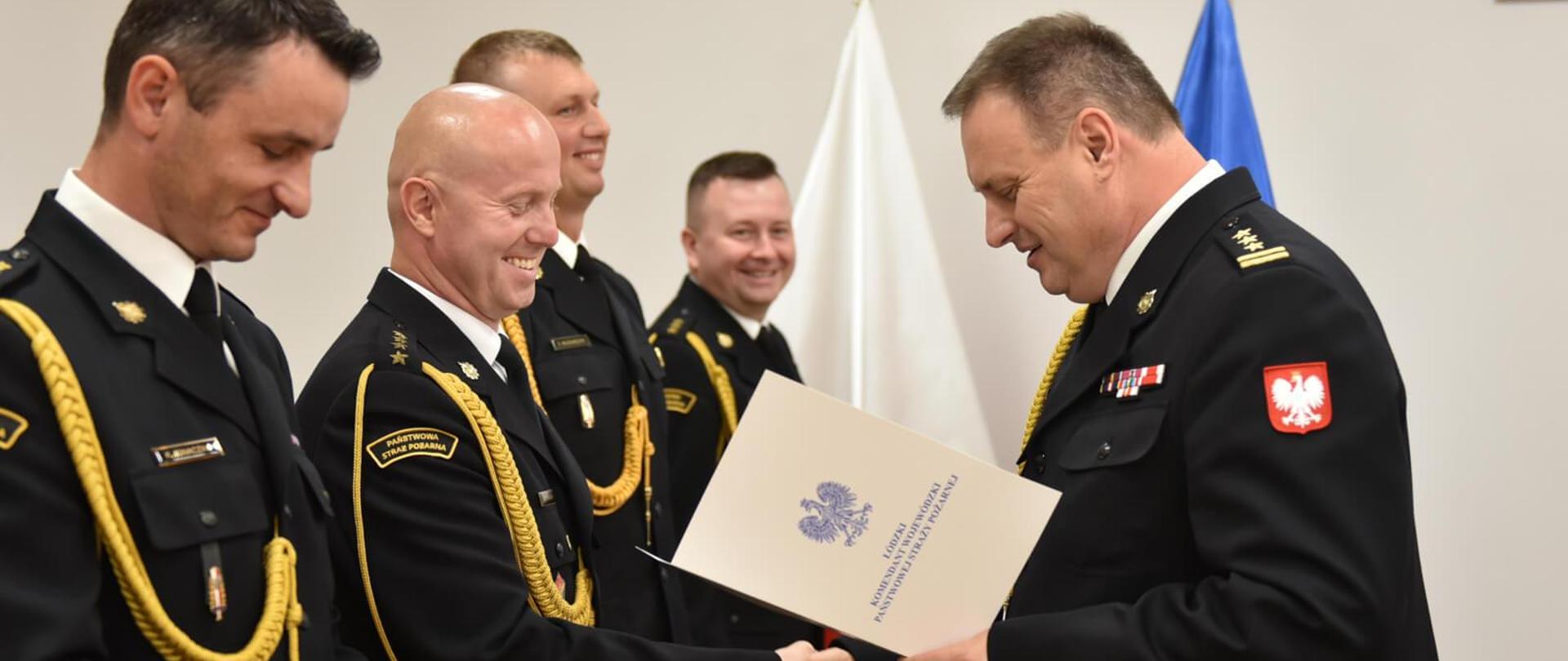 starszy brygadier Piotr Rudecki gratuluje strażakowi, w rzędzie stoi czterech strażakowi