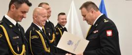 starszy brygadier Piotr Rudecki gratuluje strażakowi, w rzędzie stoi czterech strażakowi