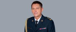 st. bryg. mgr inż. Maciej Szafarczyk w wieku ok. 50 lat ubrany w mundur galowy składającego się z białej koszuli, czarnego krawatu oraz granatowej marynarki, na której znajdują się identyfikator, złota odznaka SGSP oraz złoty sznur galowy