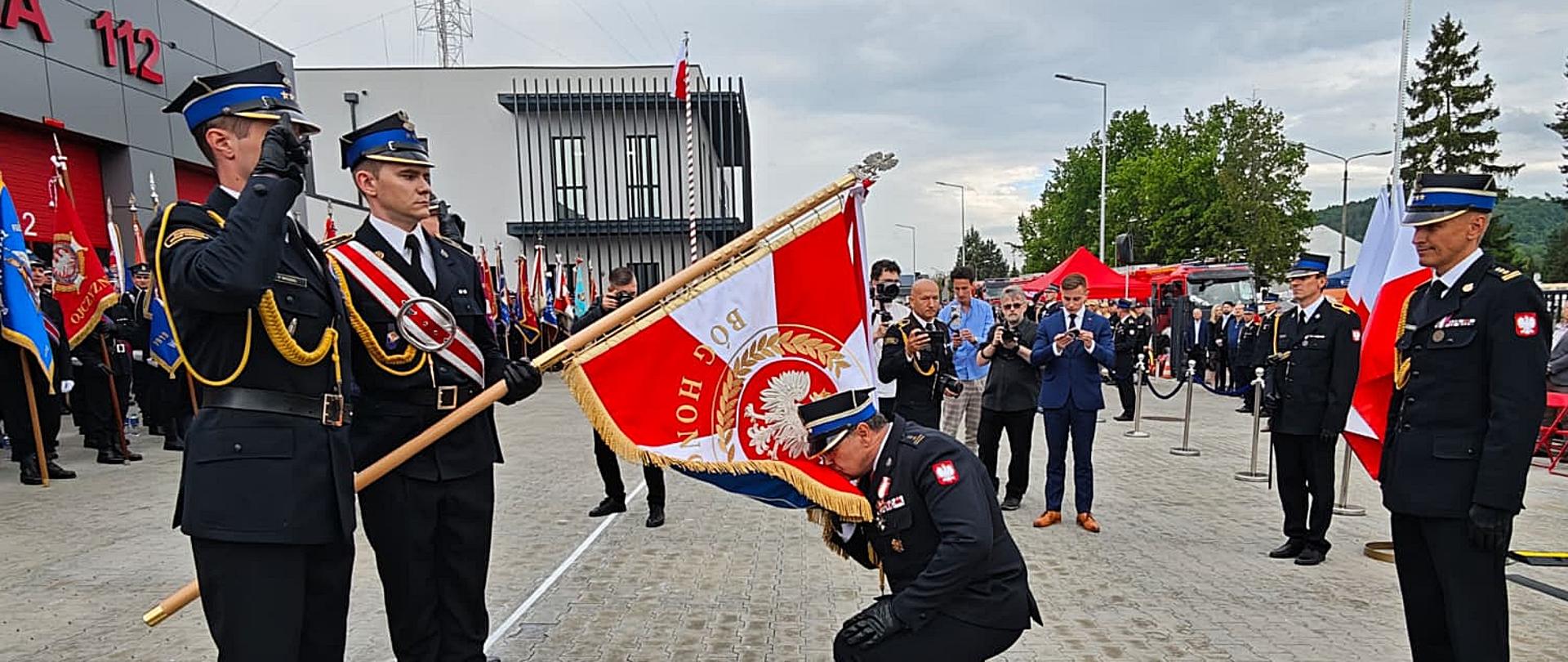 Komendant Powiatowy całuje sztandar KP PSP w Wadowicach. Po lewej stronie widzimy poczet sztandarowy, natomiast z prawej stoi Komendant Wojewódzki PSP.