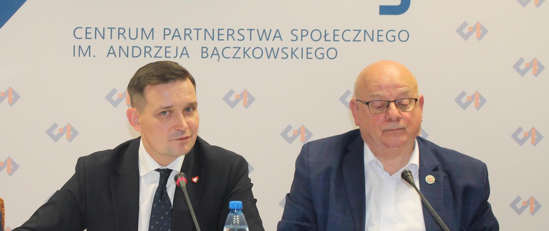 Na zdjęciu widnieje stół prezydialny za którym siedzą: Pan Michał Jaros, Sekretarz Stanu w Ministerstwie Rozwoju i Technologii oraz Pan Zbigniew Sikorski, Współprzewodniczący Zespołu ze strony związków zawodowych. W tle znajduje się baner z napisem Centrum Partnerstwa Społecznego Dialog im. Andrzeja Bączkowskiego.