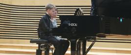 Uczeń gra razem na nauczycielką na cztery ręce na fortepianie na scenie sali koncertowej PSM