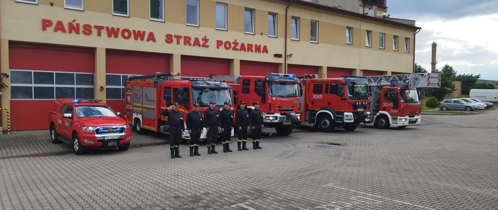 Zdjęcie przedstawia funkcjonariuszy Komendy Miejskiej Państwowej Straży Pożarnej w Kielcach stojących przed budynkami swoich jednostek na uroczystej zbiórce z okazji 81 rocznicy wybuchu Powstania Warszawskiego.