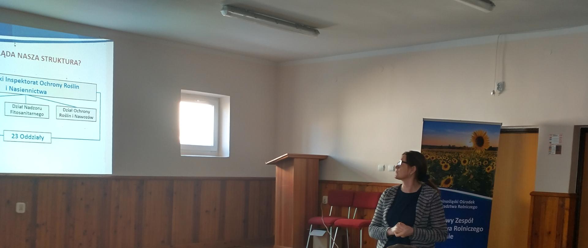 Uczestnicy szkolenia siedzący przy stole, w tle przedstawicielka Oddziału w Strzelinie patrząca w stronę ekranu z prezentacją, na której wyświetlany jest slajd ze strukturą WIORiN.