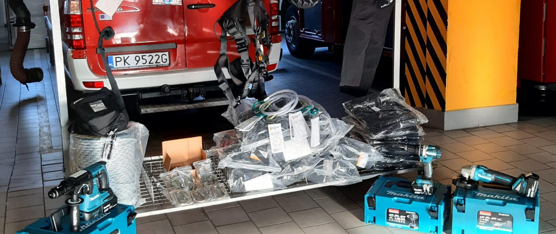 Na zdjęciu widzimy wyeksponowany sprzęt ratownictwa wysokościowego. W skład sprzętu od lewej strony kadru widzimy bezprzewodową wiertarkę udarową koloru niebieskiego firmy makita. W dalszej kolejności widzimy liny ratownicze, srebrne karabinki, czarne zawiesia, bloczki ratunkowe oraz specjalistyczne ubranie. Prawa strona kadru to bezprzewodowa wkrętarka i szlifierka kątowa firmy makita.