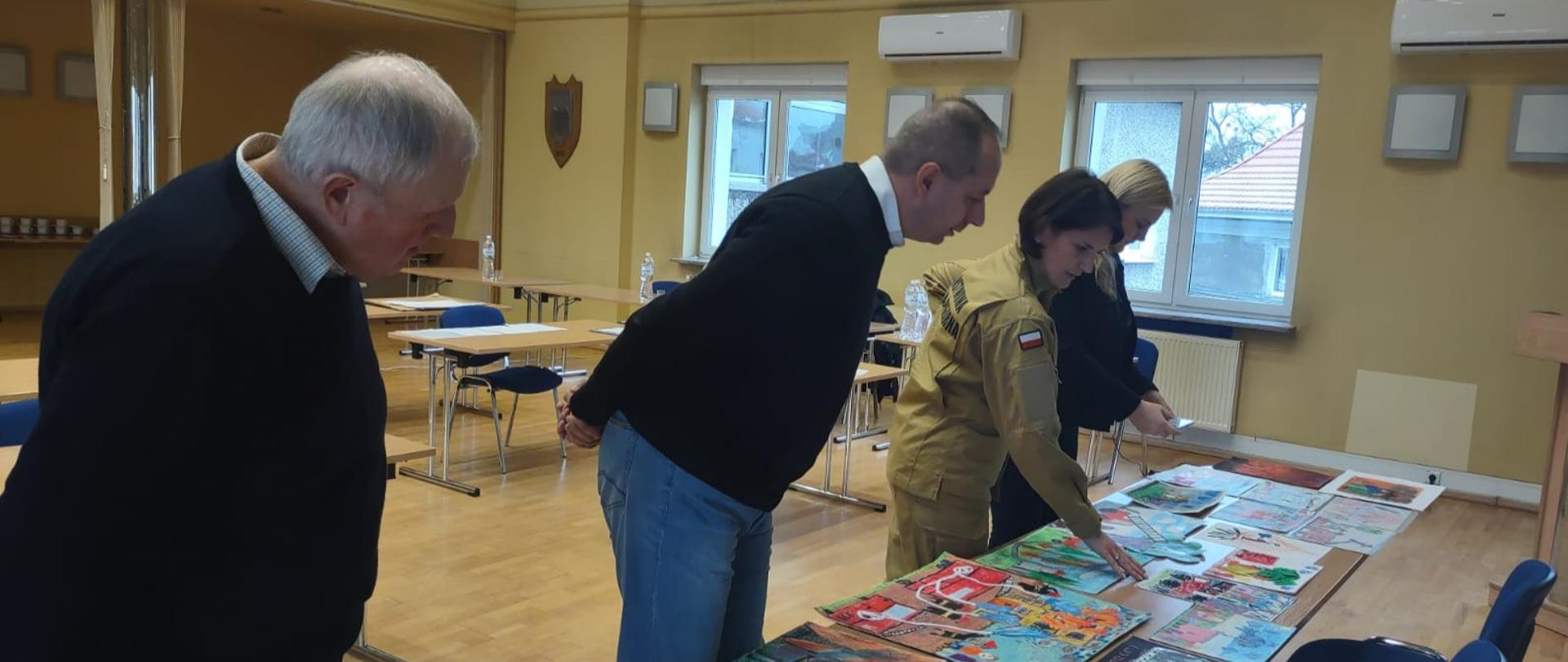 Na zdjęciu znajdują się prace dzieci na konkurs „Zapobiegajmy pożarom’’ oraz osoby oceniające prace dzieci