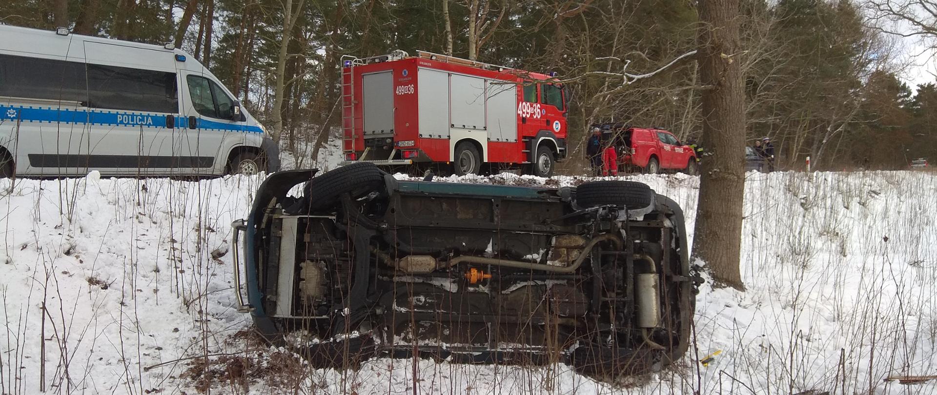 Samochód osobowy leżący na boku, pojazd policji oraz samochody pożarnicze