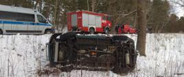 Samochód osobowy leżący na boku, pojazd policji oraz samochody pożarnicze