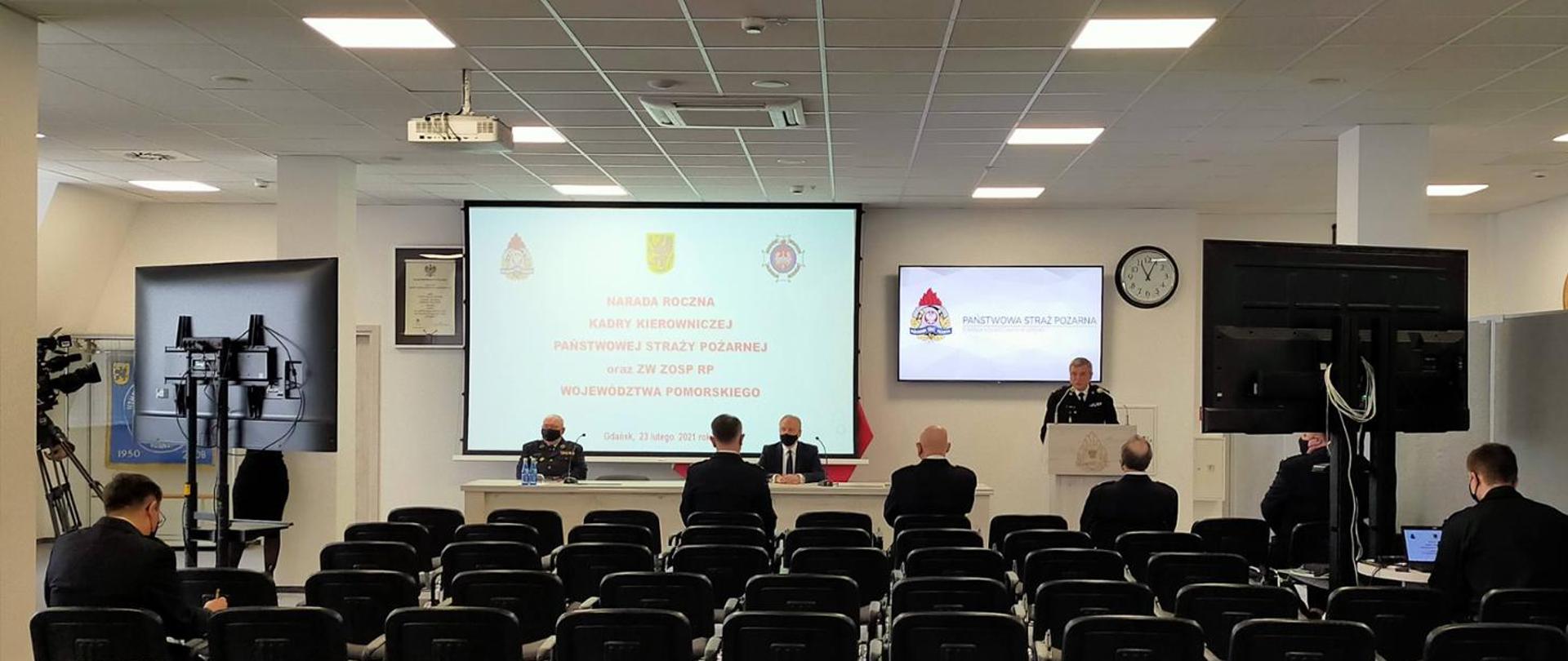 Sala konferencyjna KW PSP Gdańsk. Tyłem na krzesłach siedżą strażacy PSP oraz OSP. Przy mównicy stoi Pomorski Komendant Wojewodzki, Za stołem siedzi Wojewoda Pomorski oraz Prezes Zarządu Wojewódzkiego OSP