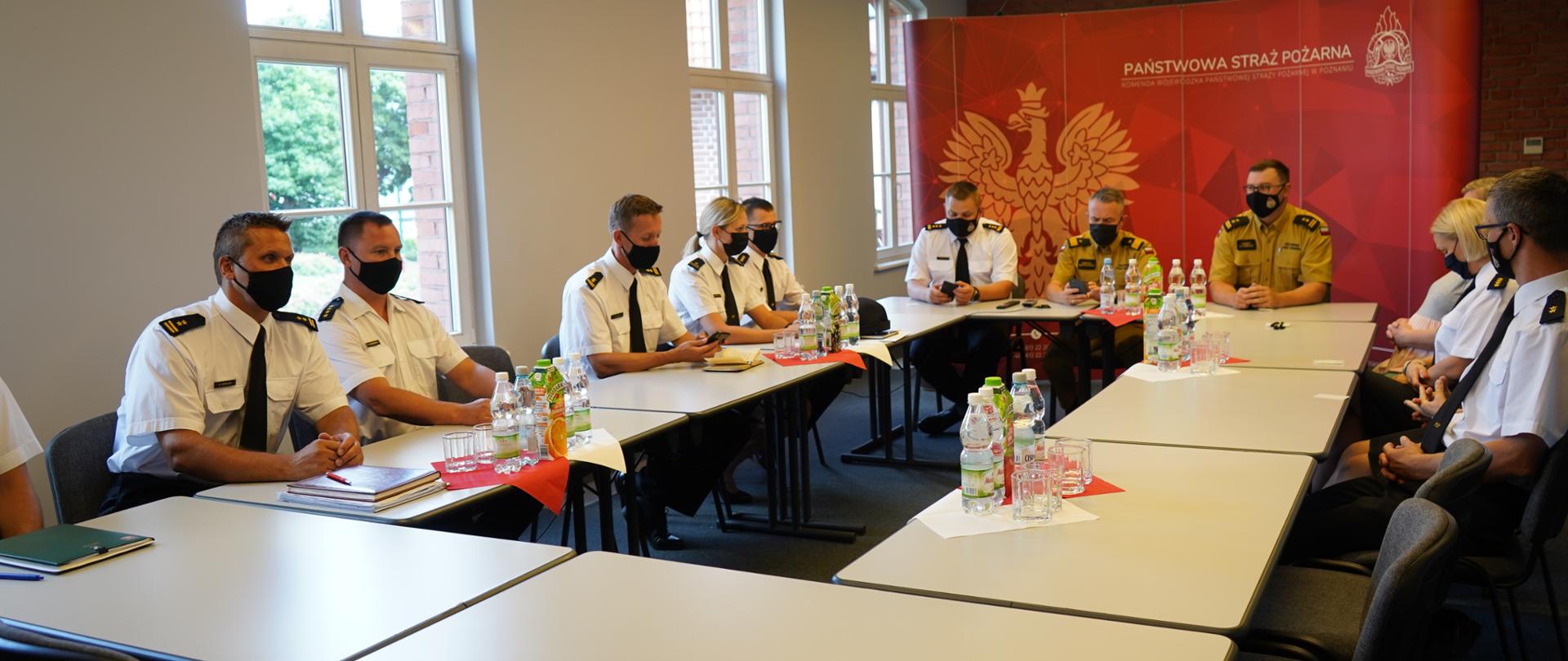 Komendant Główny PSP wspólnie z innymi funkcjonariuszami siedzą przy stole podczas odprawy służbowej 