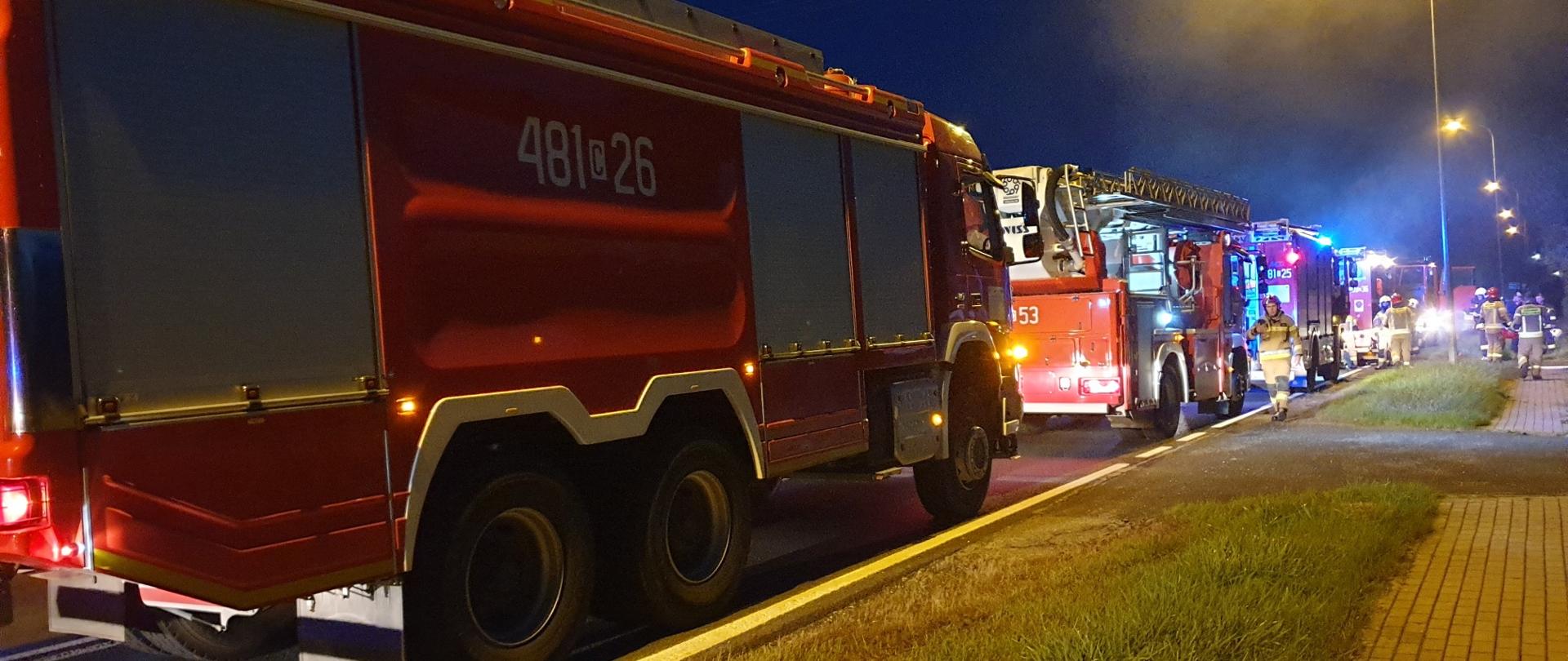 Na drodze stoi 5 samochodów pożarniczych, Obok nich stoją strażacy
