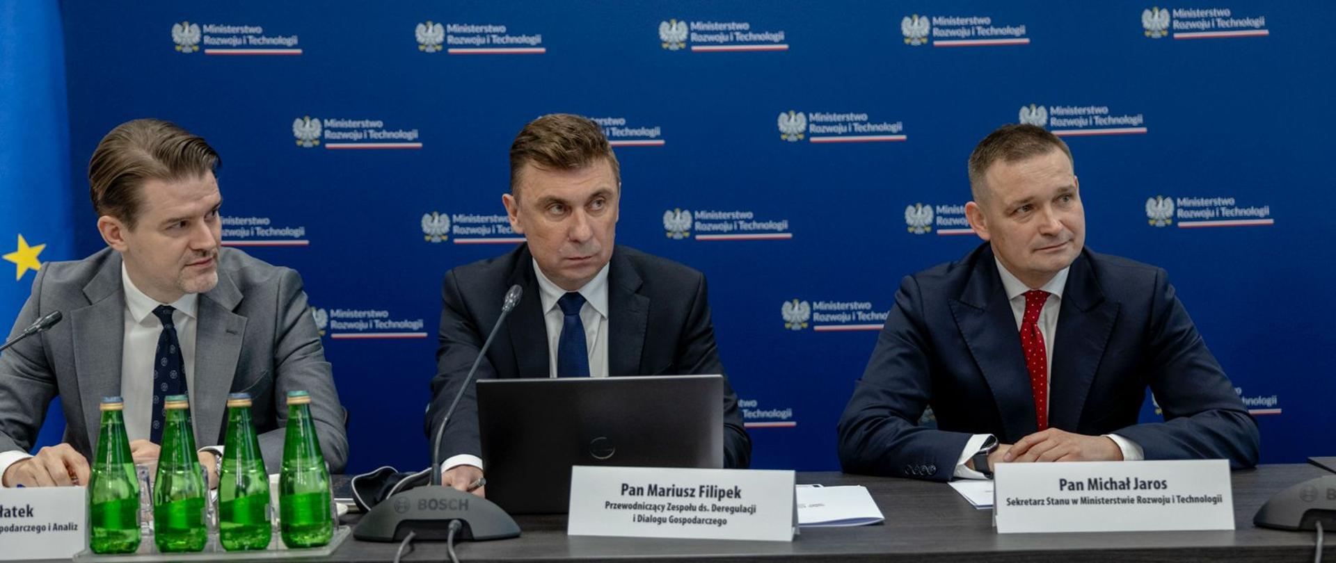 od lewej G. Płatek, M. Filipek, M. Jaros za stołem konferencyjnym. W tle niebieska ścianka z logotypami MRiT