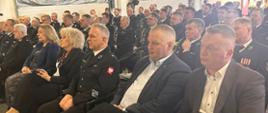 Na zdjęciu widać zgromadzonych gości oraz strażaków ubranych w mundury służbowe, którzy siedzą na krzesłach. Odprawa odbywa się w garażu siedziby KP PSP Węgrów. 