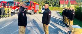 D-ca JRG składa meldunek Komendantowi Powiatowemu, w tle samochody pożarnicze