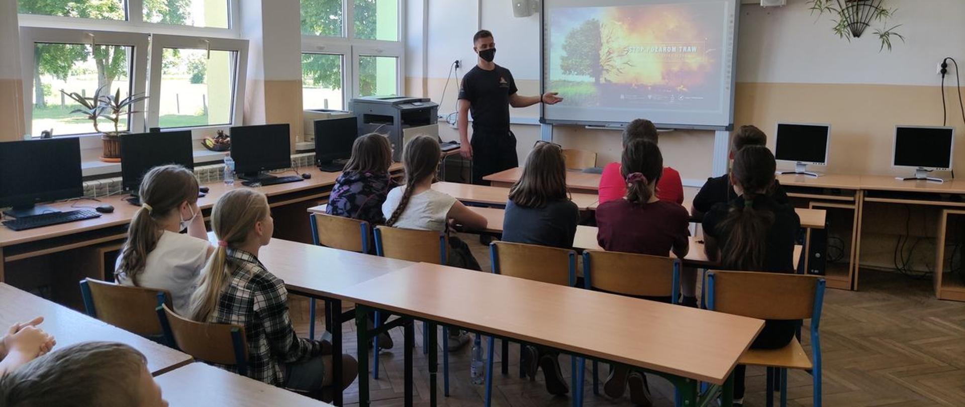 Zdjęcie przestawia funkcjonariusza Komendy Powiatowej Państwowej Straży Pożarnej w Radziejowie prezentującego informacje w tematyce zasad bezpieczeństwa pożarowego, bezpieczeństwa podczas wakacji oraz związanych z akcją „STOP POŻAROM TRAW”.