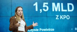 Minister funduszy i polityki regionalnej Katarzyna Pełczyńska-Nałęcz stoi na tle grafiki informującej o zainwestowaniu 1,5 mld zł z KPO