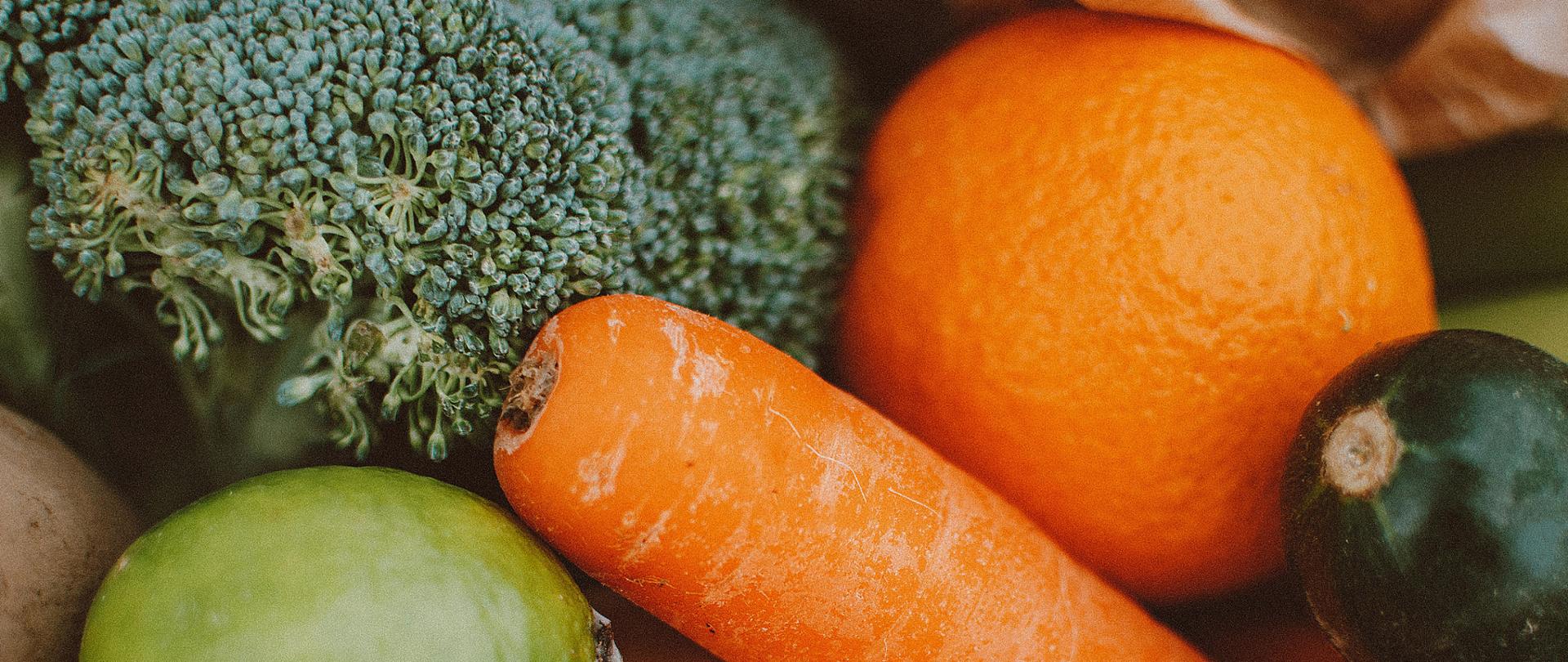 na zdjęciu warzywa i owoce w skupisku, na pierwszym planie pomarańczowa marchew, poza tym pomarańcza, ogórek i kalfior