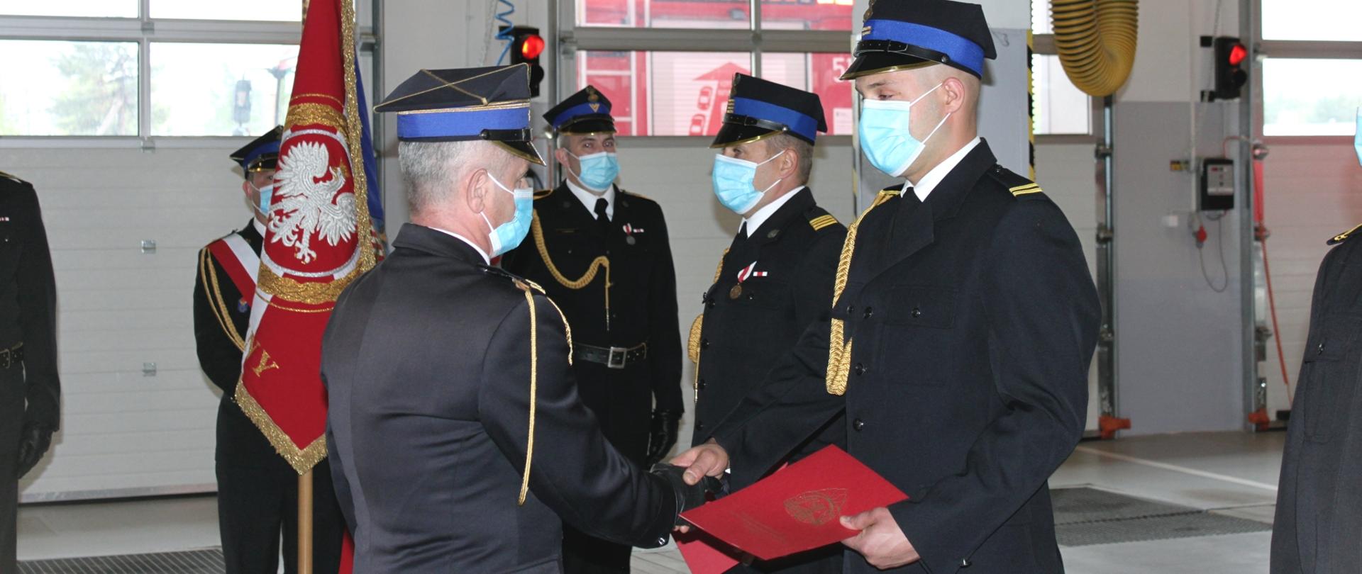 komendant powiatowy wręcza strażakowi akt mianowania na wyższy stopień służbowy w tyle poczet sztandarowy strażacy w mundurach wyjściowych