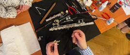 Prowadzący warsztaty prezentuje proces konserwacji instrumentu - zdjęcie przedstawia rozłożoną na stole szmatkę filcową, na której umieszczone są części fletu oraz specjalistyczne narzędzia 