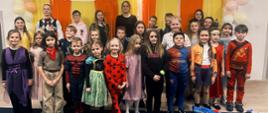 Dzieci i młodzież w barwnych przebraniach karnawałowych stoją razem na scenie, prezentując różnorodne stroje i wyrażając radość ze wspólnego świętowania