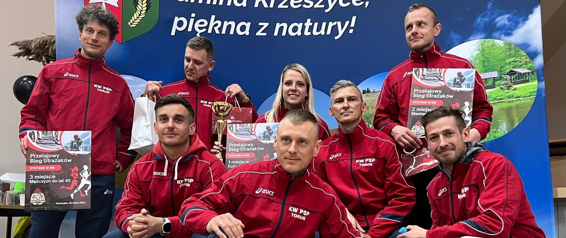 8 zawodników w strojach sportowych z pucharami i dyplomami pozujących do zdjęcia