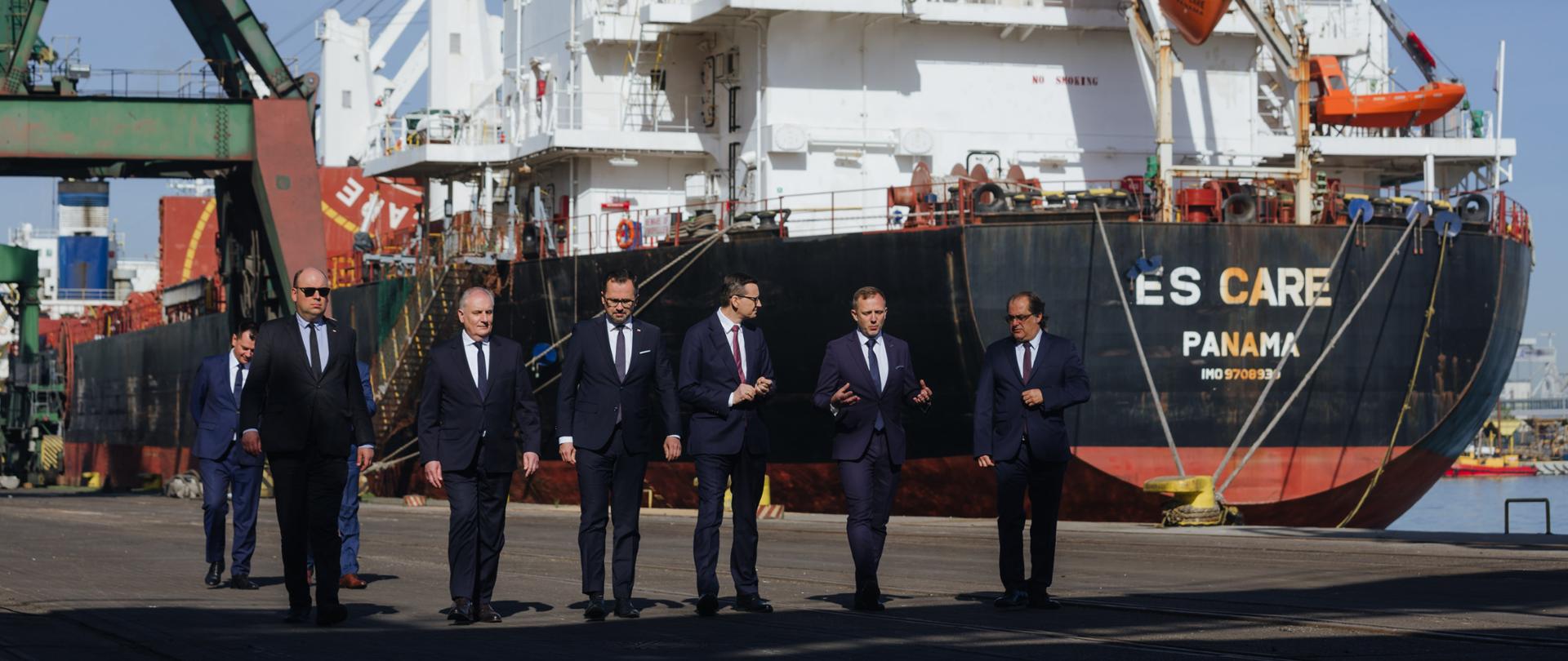 Premier oraz delegacja idą na tle statku.