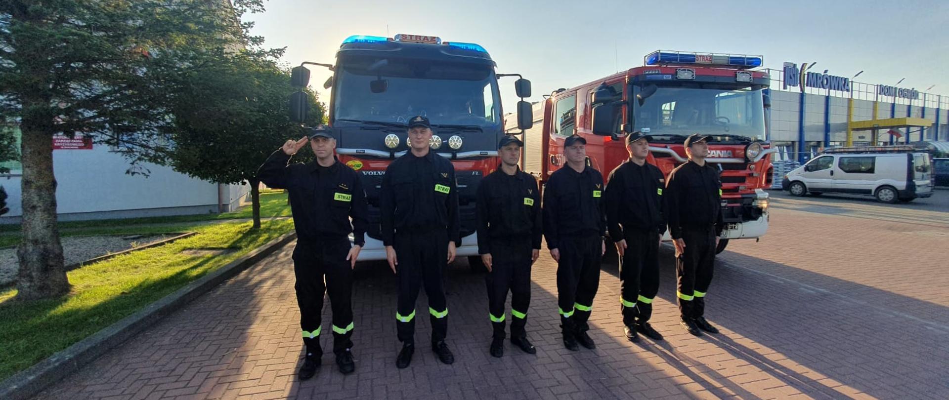 Zdjęcie przedstawia strażaków oddających hołd zmarłemu strażakowi OSP. Stoja przed wozami strażackimi na baczność.