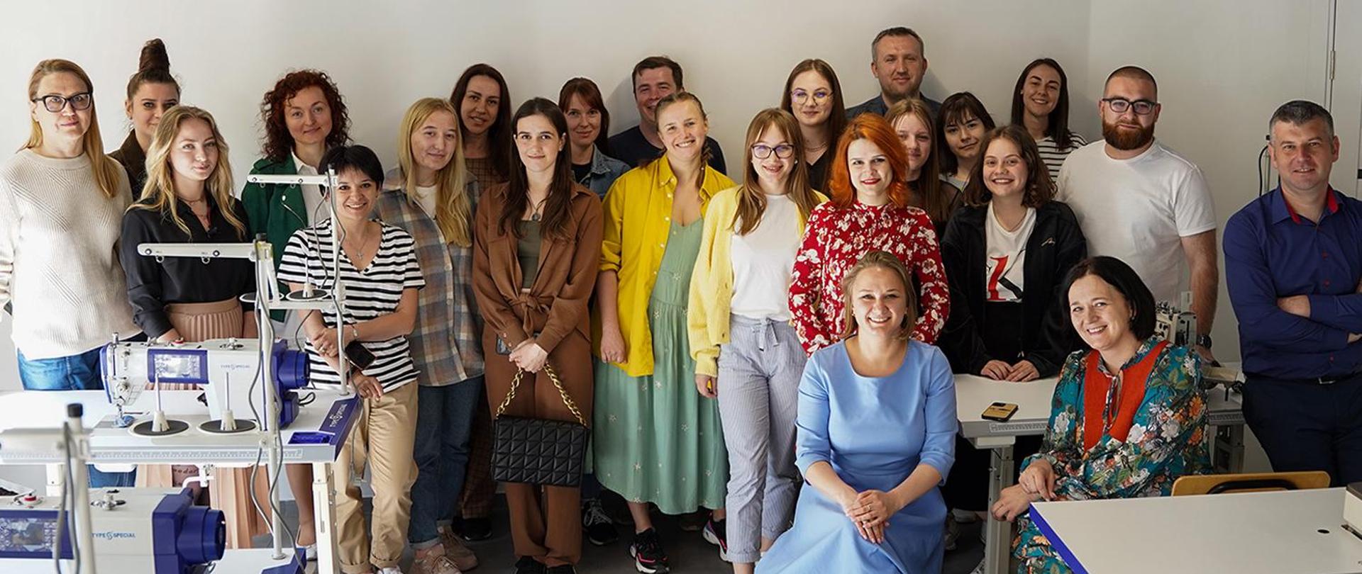 Kilkanaście osób pozuje do zdjęcia w zakładzie krawieckim.
