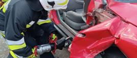 Zdjęcie przedstawia strażaka podczas cięcia progu samochodu osobowego nożycami hydraulicznymi 