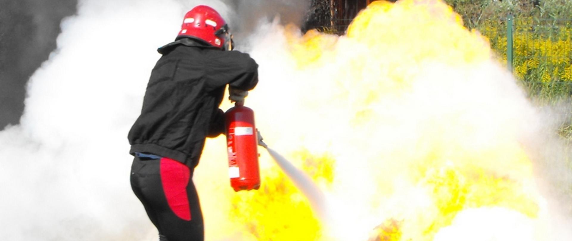 Zdjęcie przedstawia strażaka gaszącego podczas ćwiczenia bojowego