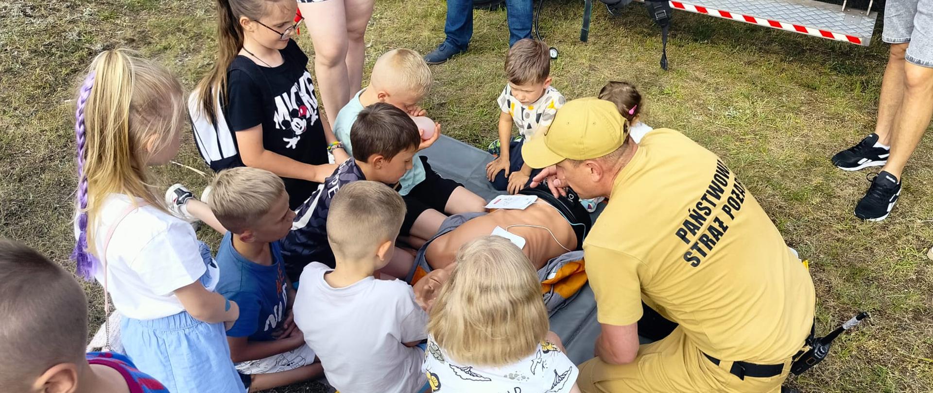Strażak pokazuje jak prowadzić masaż serca na manekinie dzieciom.