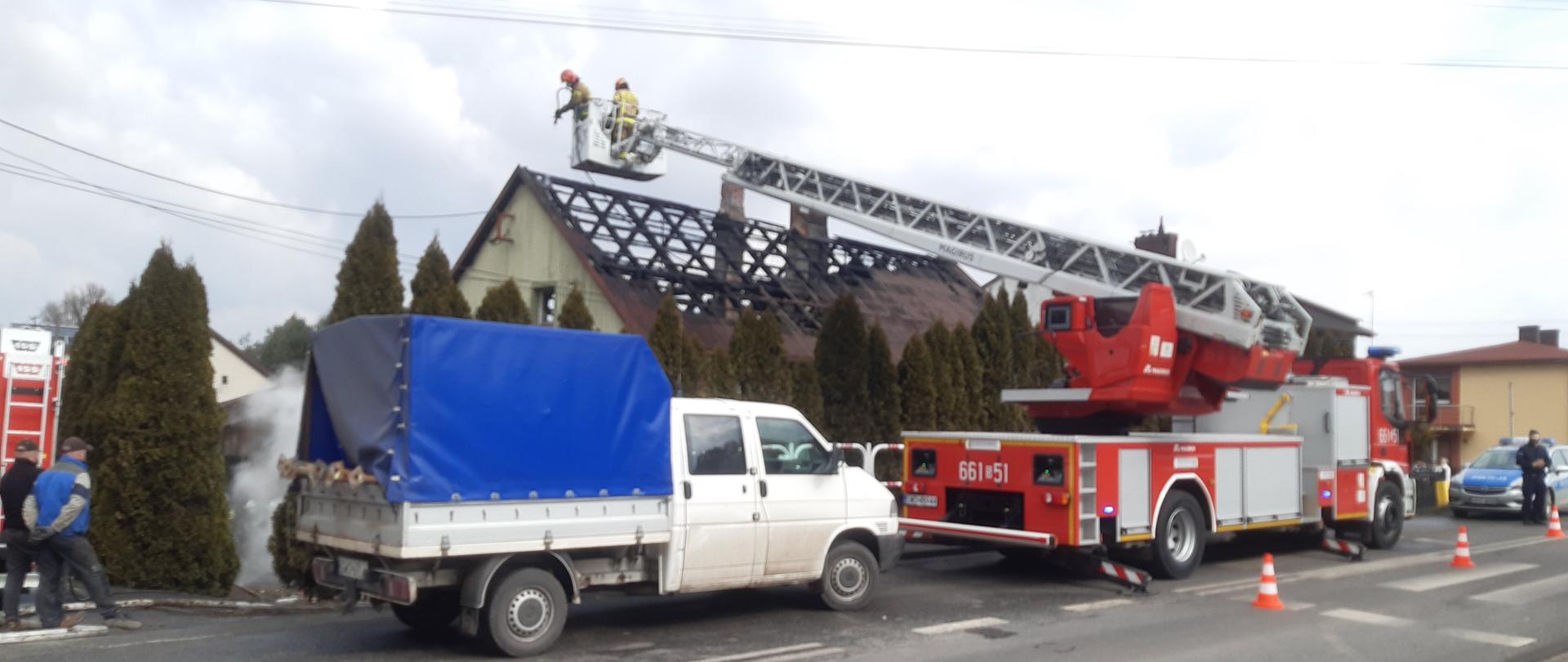 Na zdjęciu widać drabinę mechaniczną pożarniczą ze strażakami na tle palącego się budynku