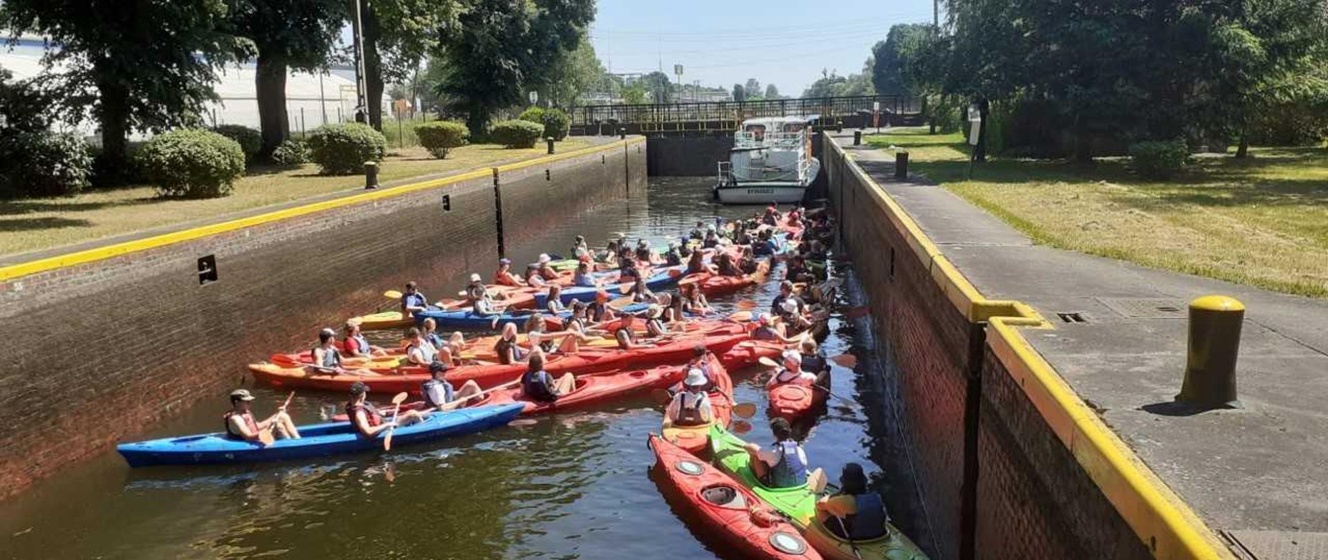Prądy (śluza nr 5) drogi wodnej Wisła-Odra, będąca elementem międzynarodowej drogi wodnej E-70. W komorze śluzy wypełnionej wodą na pierwszym planie znajduje się grupa kajakarzy oraz statek. Woda w śluzie podnosi się. Trwa śluzowanie. Po napełnieniu wrót wodą, wrota zostaną otwarte i wszyscy wodniacy popłyną w dalszą drogę rzeką Notecią. 